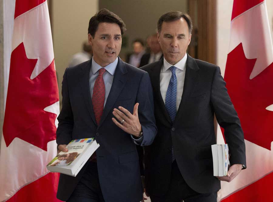 Trudeau and Morneau walk side-by-side with Canadian flags on either side of them.