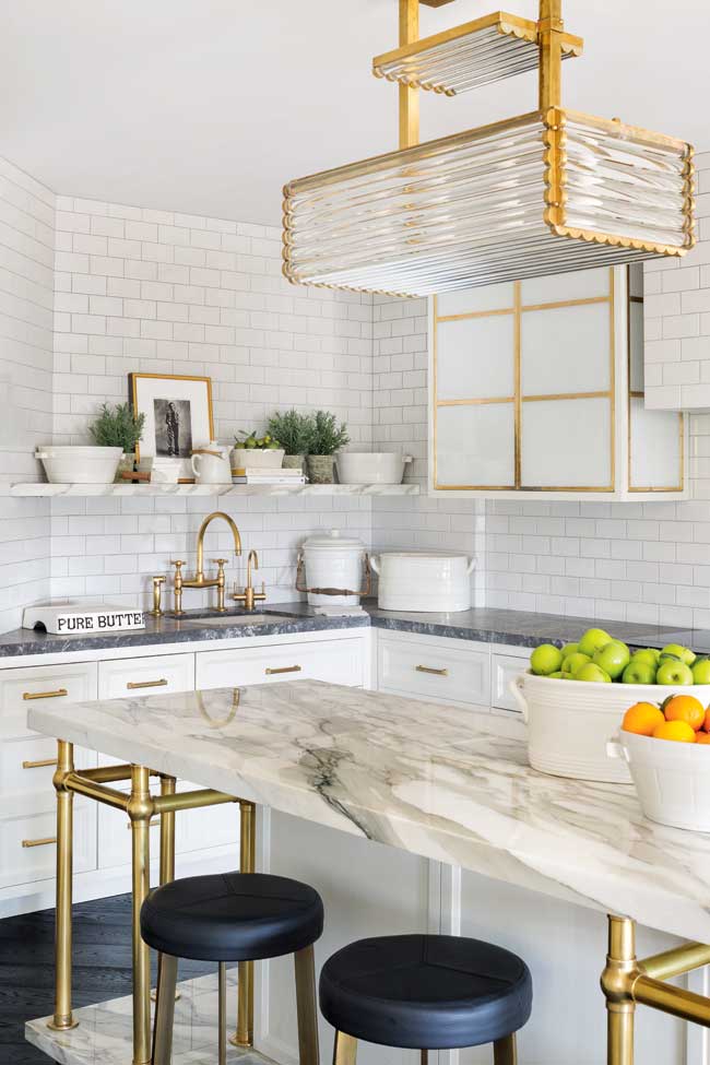 A mostly white kitchen with a marble island and gold accents.