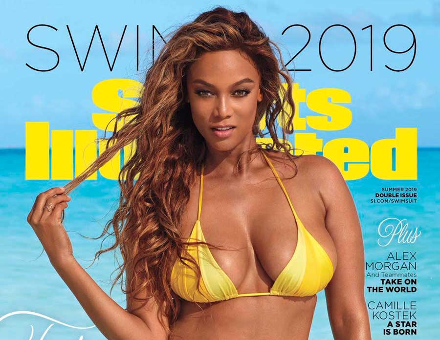 Tyra Banks holding a few strands of hair between her fingers wearing a yellow bikini.