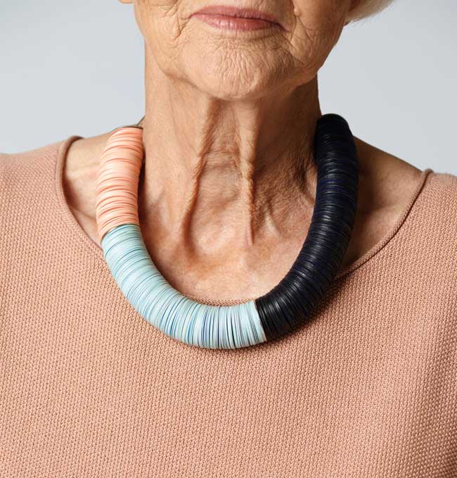 A woman wearing a thick necklace in peach, pale blue and black.