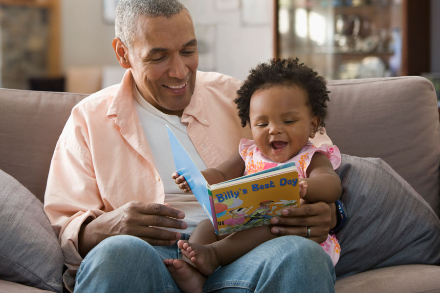 A man with greying hair reading a children's book to a toddler.