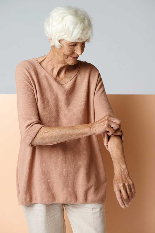 A woman wearing a dark peach top, rolling her sleeves up.