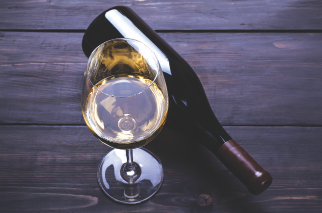 A photo of a glass of white wine with a wine bottle laying on its side next to it.