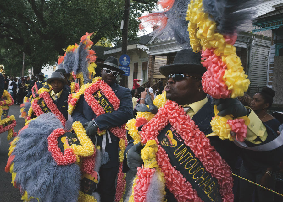 A picture of three men in suits with colourful signs marching in a traditional first line parade.