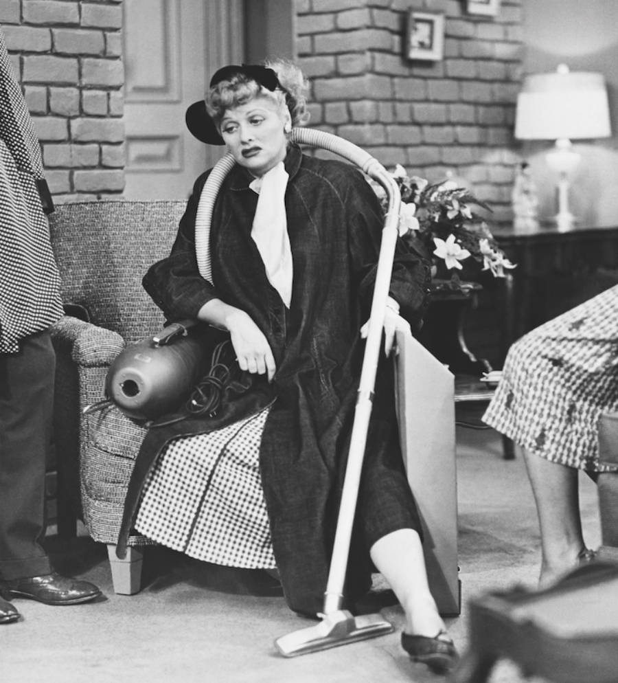 A photo of Lucille Ball looking tired on a chair with a vacuum hose draped around her shoulders.