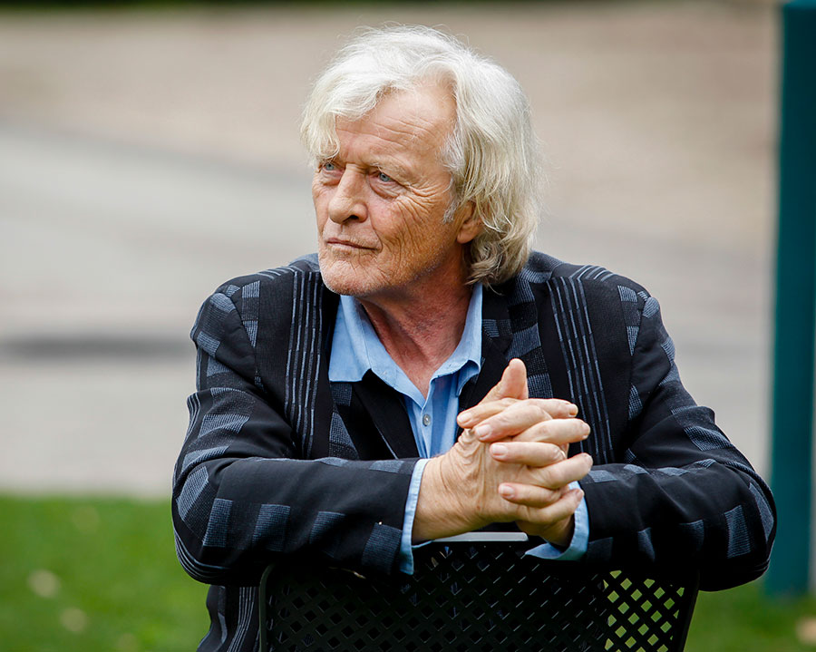 Rutger Hauer sitting backwards on a chair with his hands resting on the backrest.