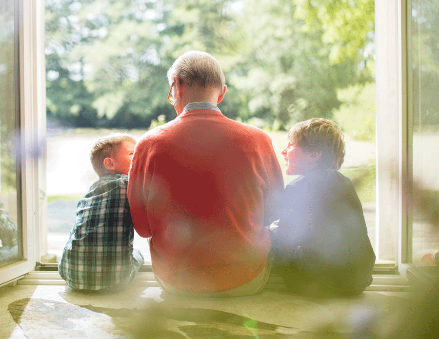 A grandfather and his two grandsons sit on the doorstep leading out to the backyard.