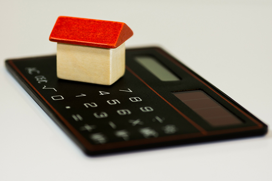 A picture of a small wooden toy house sitting on a calculator.