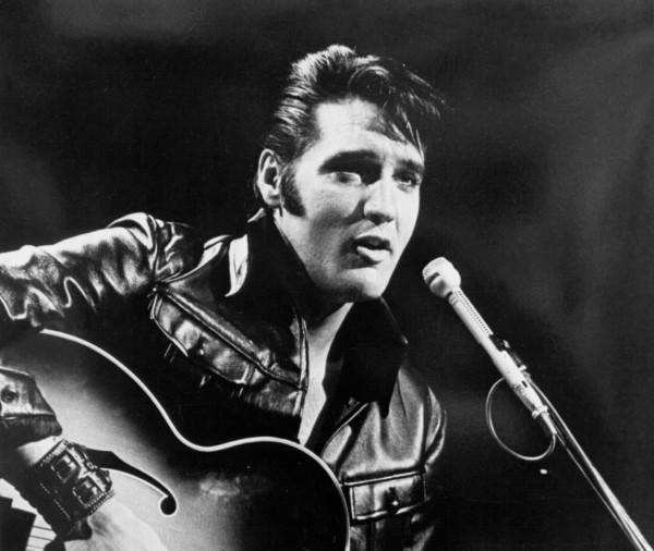 Elvis Presley strumming his guitar as he sings into a microphone.