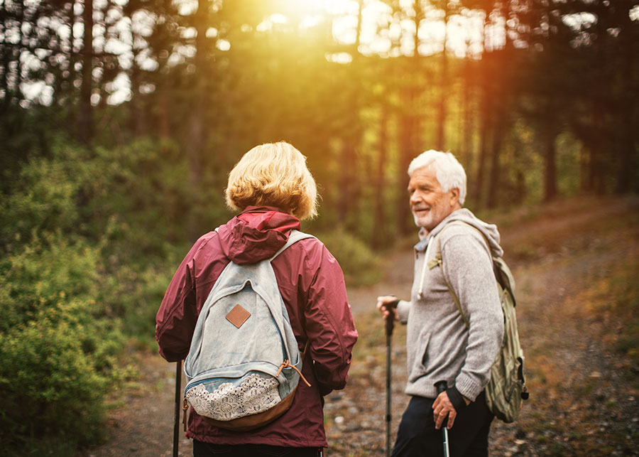 A gray haired man hiking through the forest with a woman.