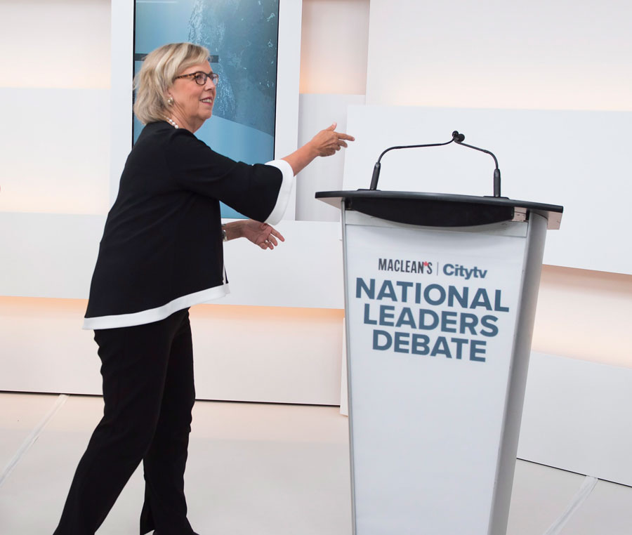 Green Party Leader Elizabeth May, left, reaches to the empty mic stand where the invited Liberal Leader Justin Trudeau turned down the debate.