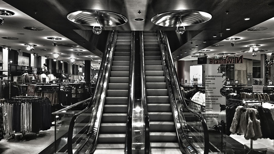 Black and white photo of escalator at department store.