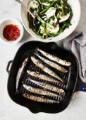 A frying pan full of sardines with a bowl of salad sitting next to it.