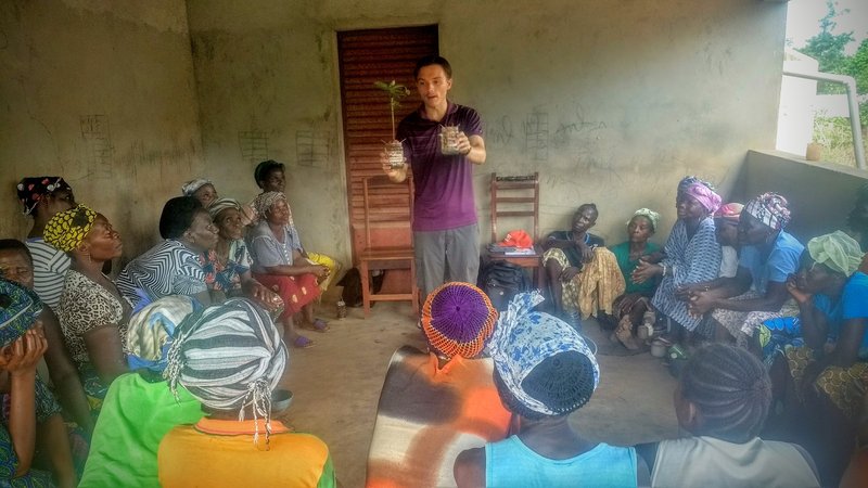 A young male Volunteer holds a sapling in the middle of a classroom while teaching