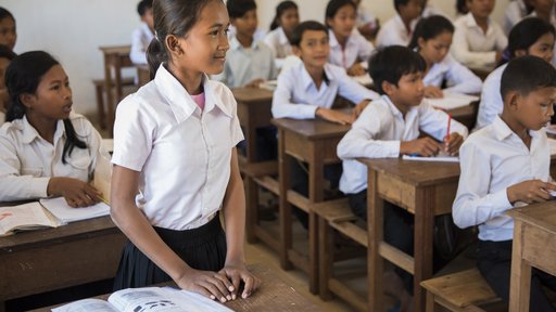 Girl standing at her desk in a classroom in Cambodia.