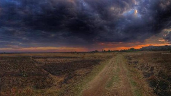 A colorful and beautiful picture of Malawi's landscape. Mountains in the distance are covered by dark clouds as a dirt path l