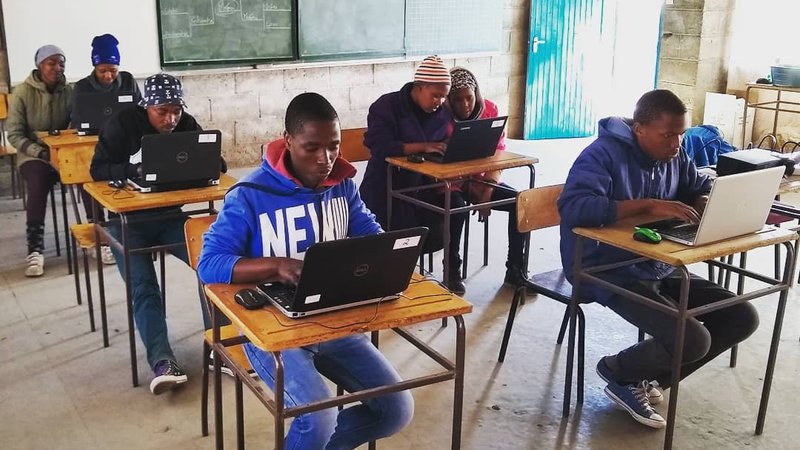 Young African adults it at desks, working on computers, in the computer lab.