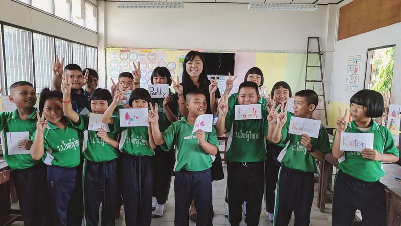 Volunteer Andrea poses with a class of primary school kids. They all hold up homemade name tags and peace signs.