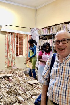 A man stands behind stacks of paper files.