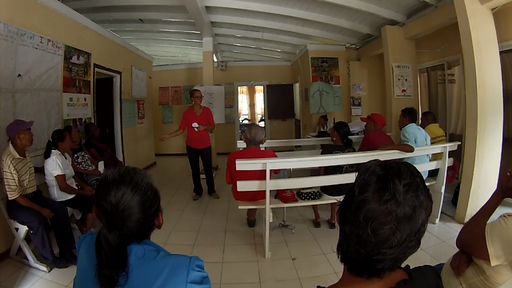 People stand and sit in a room listening to health care workers give lessons.