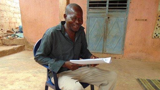 Mahamadou Coulibaly, a Senegalese national and Peace Corps counterpart, sit on a chair outside holding a report.