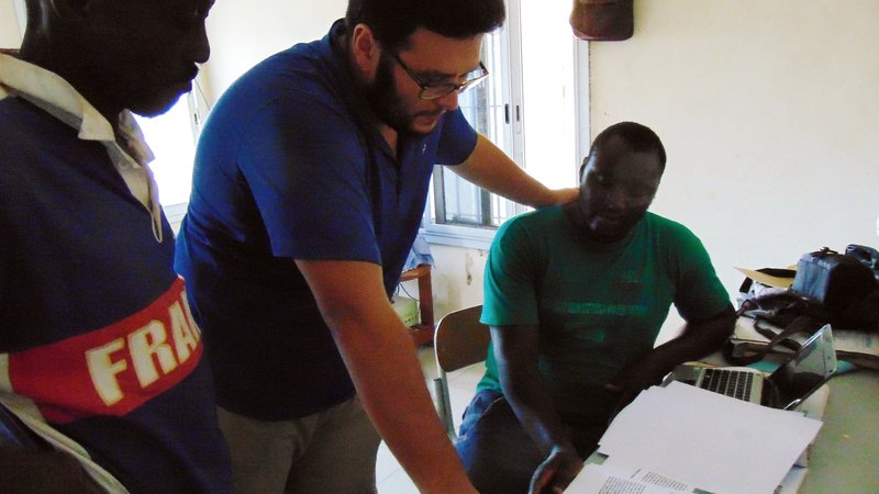 A male Peace Corps Volunteer points out data points to a male Senegalese coworker.