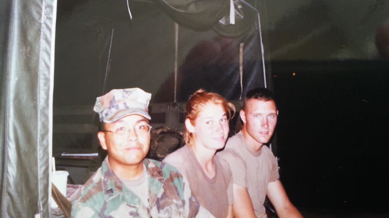 An American female Marine smiles while sitting on the back of a truck with a fellow American and a Thai national in army fatigues.