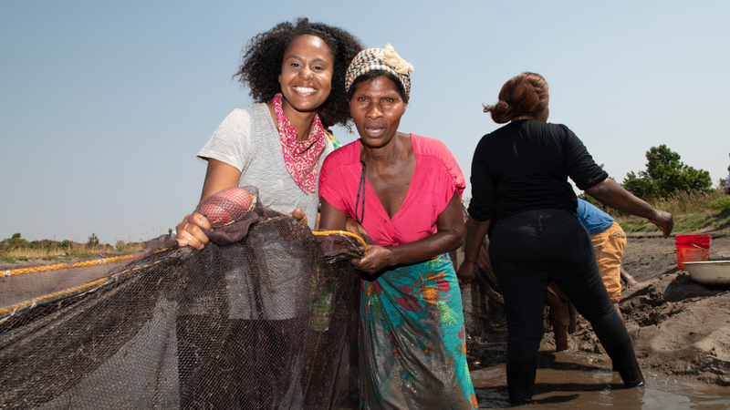 An African-American Peace Corps Volunteer (left) stands with a Zambian woman. They are holding a large fishing net.