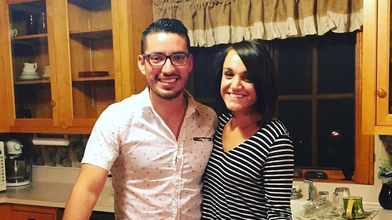 A Peruvian man and a white woman stand together by a table and smile