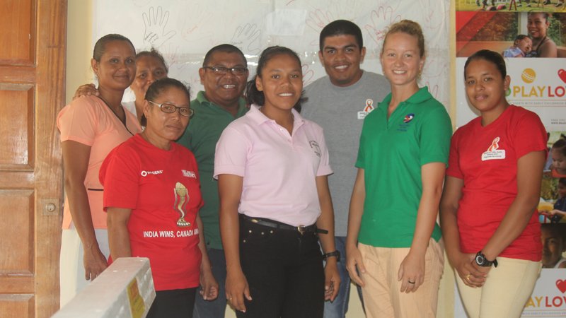 A female Volunteer stands smiling with her Guyanan coworkers inside of a health clinic.