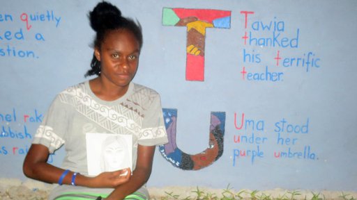 Student Elema Wilson holds her original artwork beside the final product in the letter U from the alphabet wall.