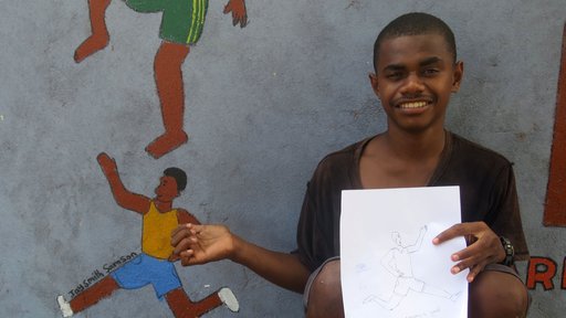 Student Jaysmith Samson holds his original artwork beside the completed picture of the healthy and fit section of the mural.