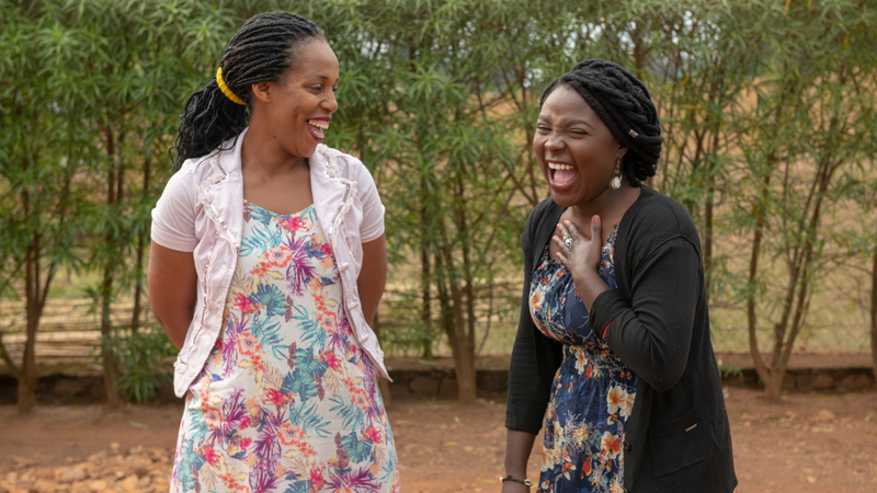 Two black women stand beside each other, smiling and laughing.