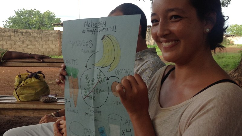 A female Volunteer sits outside and hold up a drawing of nutritious foods and moringa
