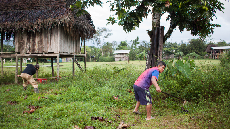Two men garden in a field with a house in the background.