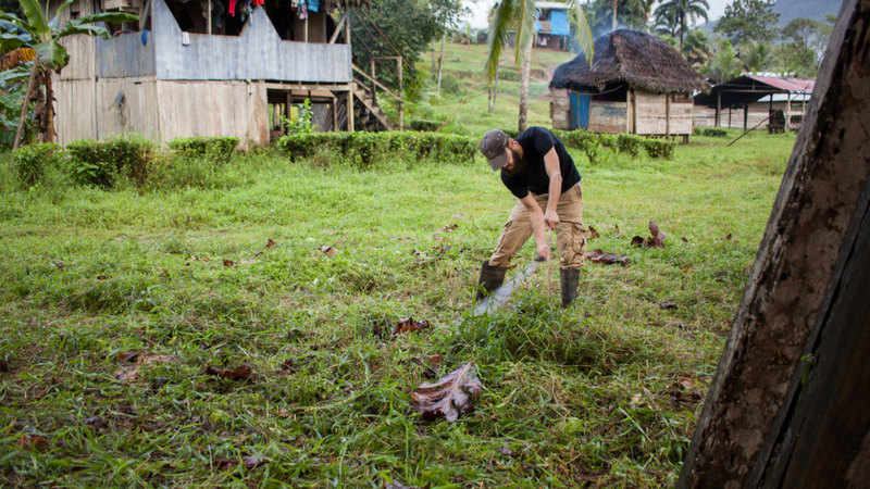 A man gardens in a field with a house in the background