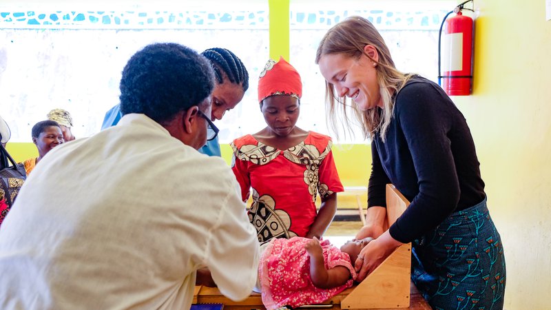 PCV Grace and community health workers measure a baby with the help of mom