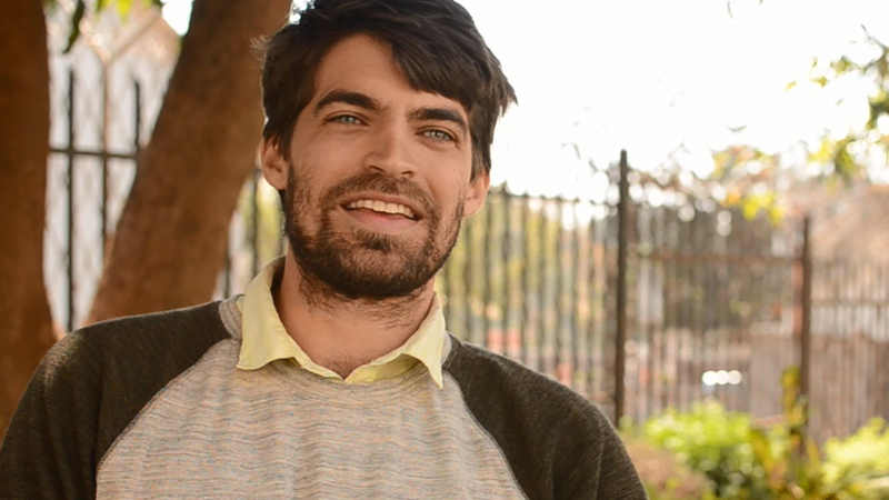 Peace Corps Malawi's Volunteer Support Assistant, Paul, smiles at the camera wearing a beige and green shirt.