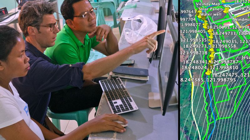 A American male sits with Filipino colleagues looking at a data map on a computer