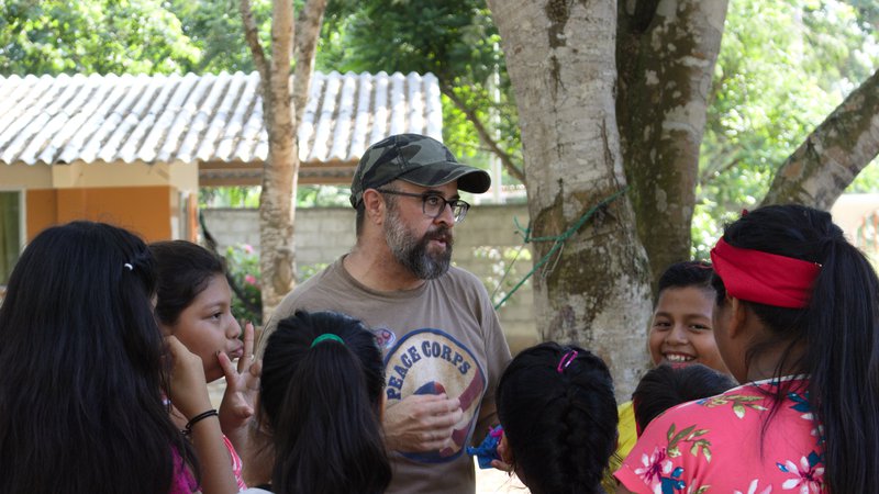 Hispanic male volunteer with beard talks with group of Ecuadorian students outside by a tree