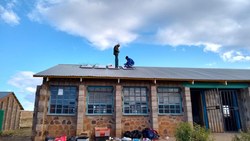 Two African men install solar panels on a school roof in Lesotho