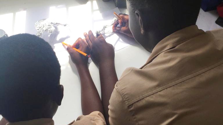 Two Jamaican students sitting down at a table constructing a sculpture made out of foil and drawing out the design