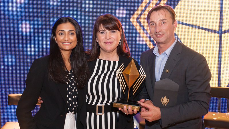 Two women and a man stand together holding an award.