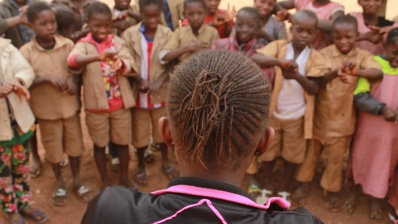 The back of a female member of a youth club can be seen as she leads a handwashing demonstration for young primaty school stu