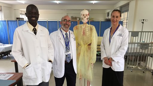Global Health Service Partnership Volunteers and a faculty member of the nursing department, dressed in lab coast, stand next to a skeleton.