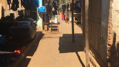 A classic Malawi market, complete with items to buy, thatch stands, and a dirt path in between.