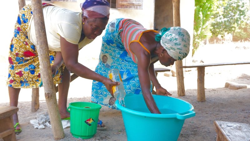 Bitho adds water to the soap mixture while Kotoko stirs. The process takes about one hour spread over two days and is much easier with a group of women.