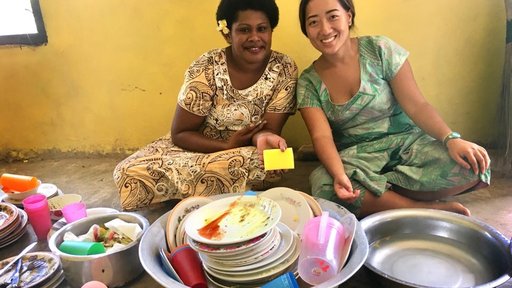 Asian Pacific American Volunteer sits with Fijian woman washing dishes